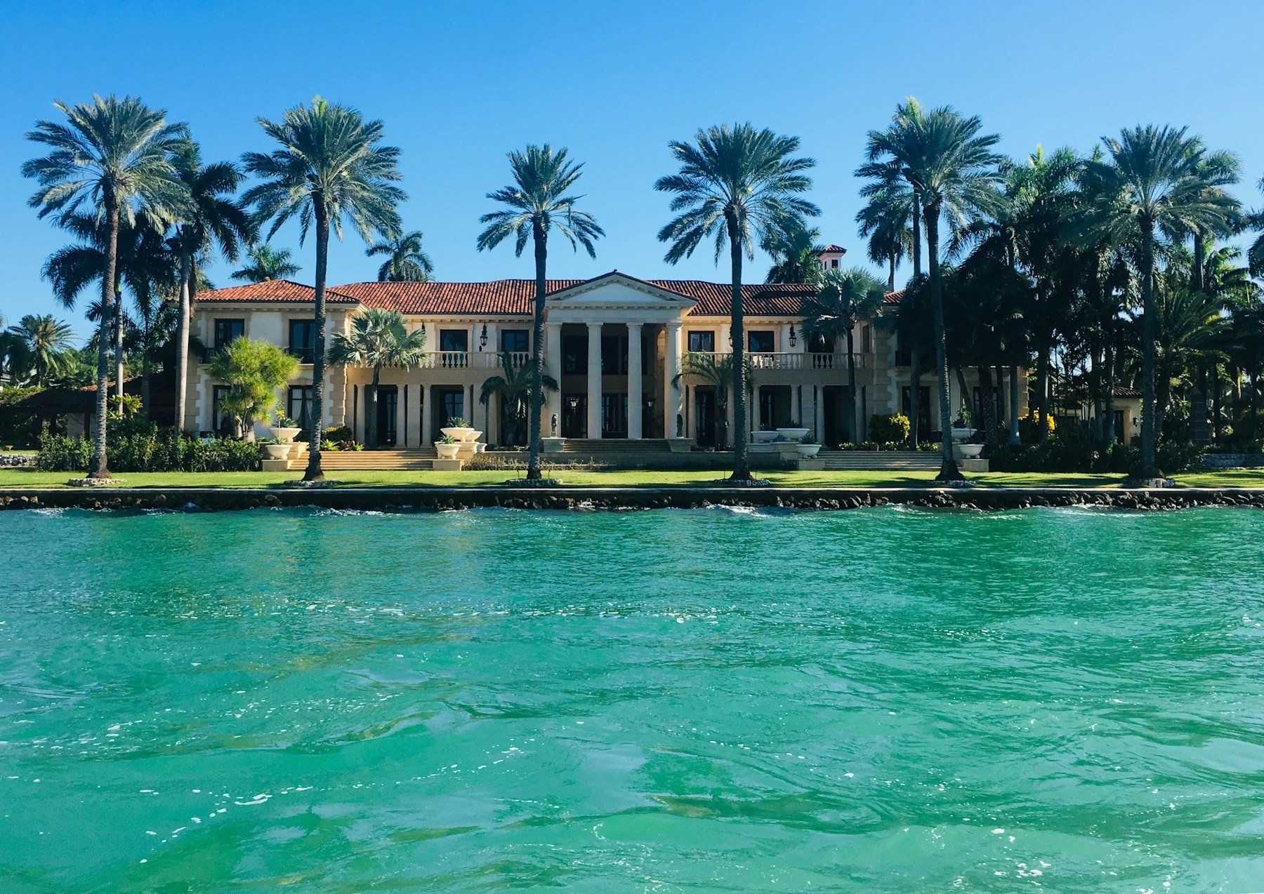 The Waterside Cottage from the street, a single-storey house with a tile roof and palms
